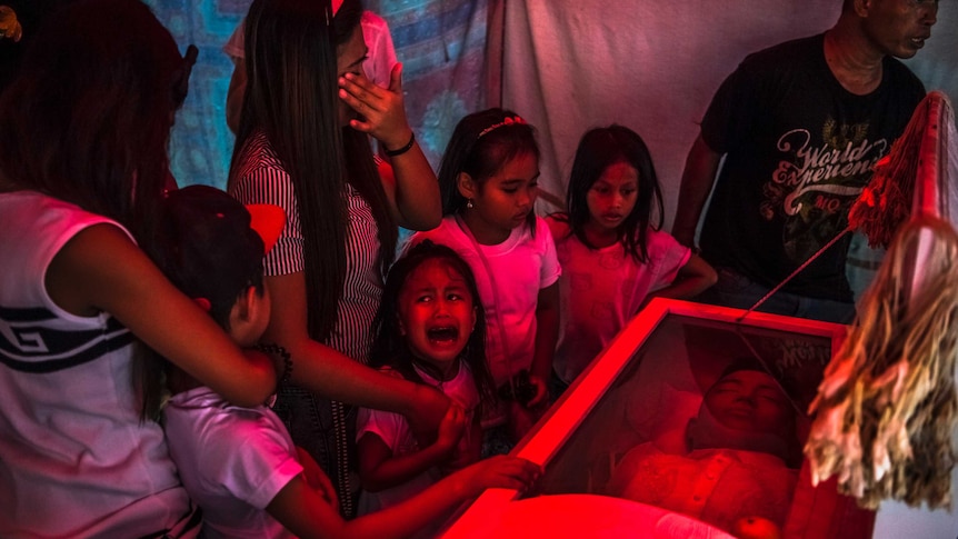 A girl stands with her family crying at her fathers burial in Manilla