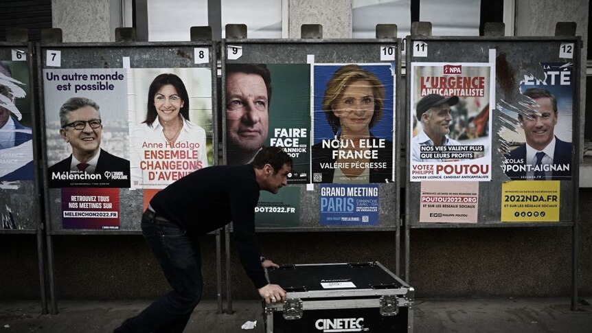 A technician pushes a flight case past campaign posters of presidential candidates in Bordeaux, southwestern France,
