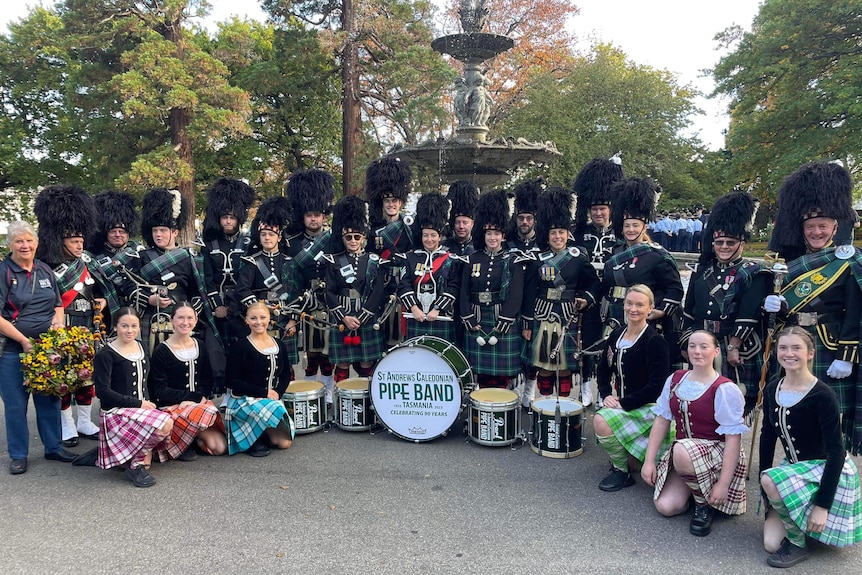 Bagpipe band and Scottish dancers pose in front of a fountain