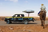 A man rides a camel next to a truck with an aircraft missile launcher welded to the back.
