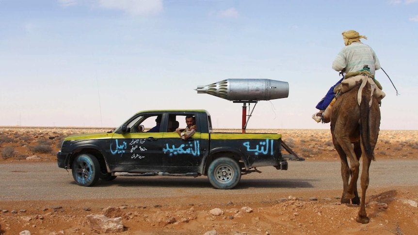 A man rides a camel next to a truck with an aircraft missile launcher welded to the back.