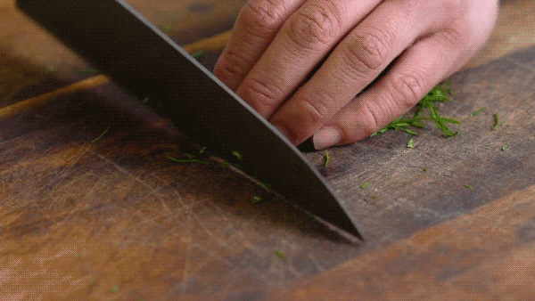 Thi Le finely slices herbs with a chef's knife.