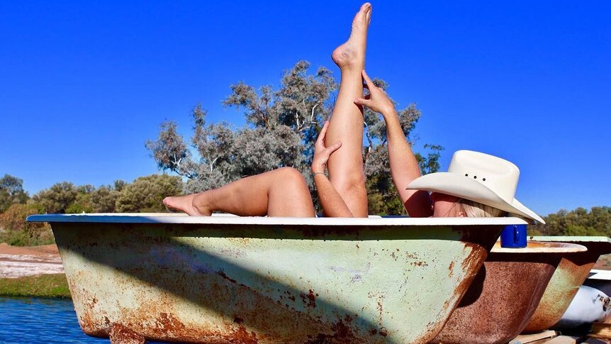 Woman in cowboy hat sits in outdoor bathtub