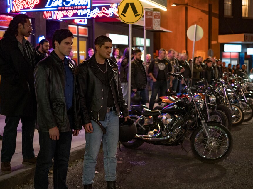 Several men standing around with multiple motorcyles parked and bright lights