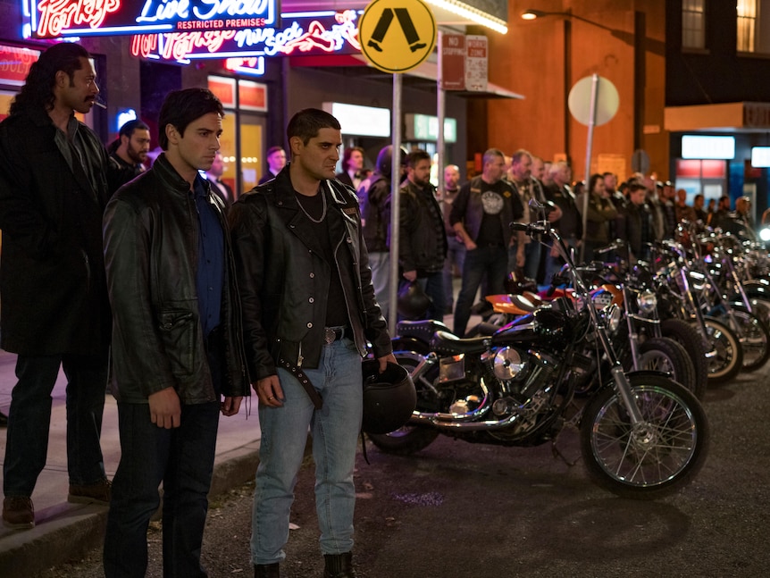 Several men standing around with multiple motorcyles parked and bright lights