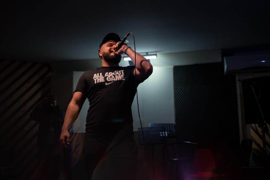 A man holds a microphone to his mouth, in a mostly darkened room.