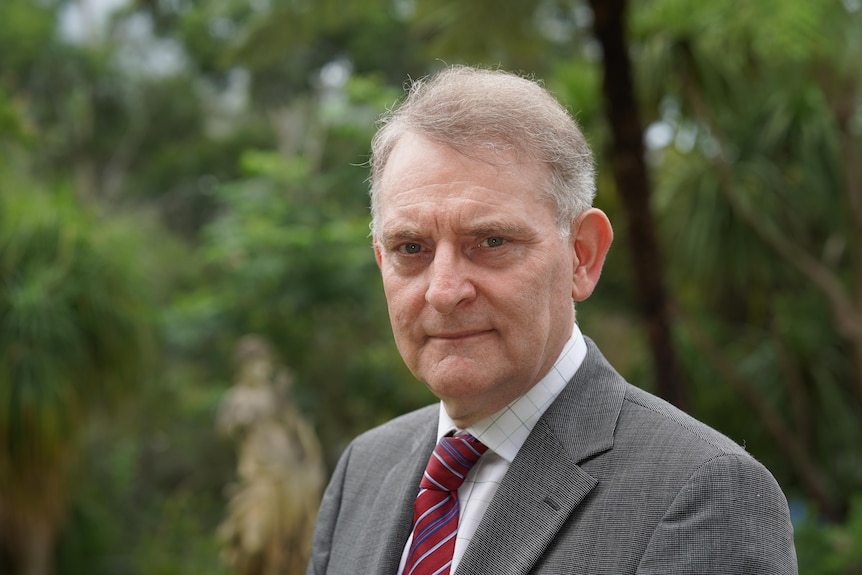 A man in a suit stands outdoor.