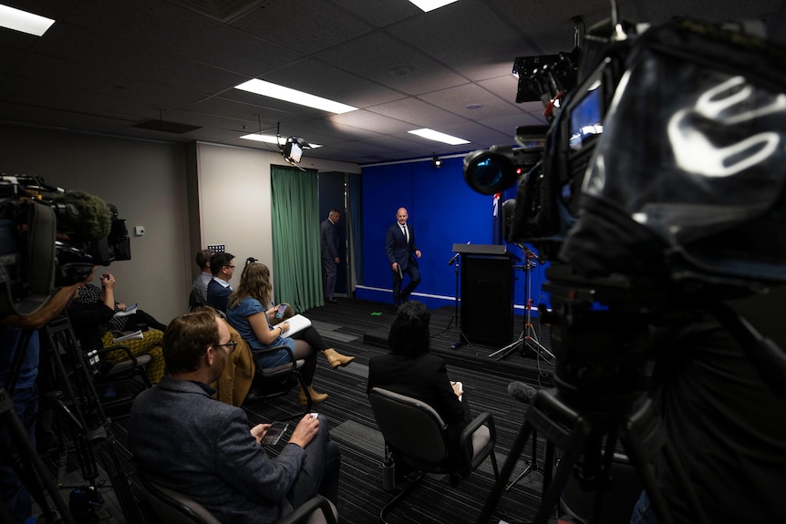 Two men walking into a room of waiting media representatives