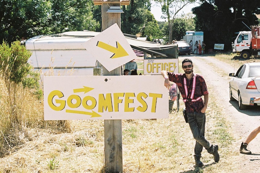 A man stands next to a goomfest sign