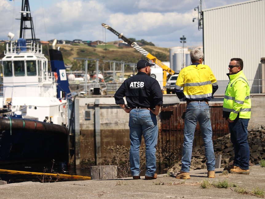Three men at the site of a tugboat mishap.