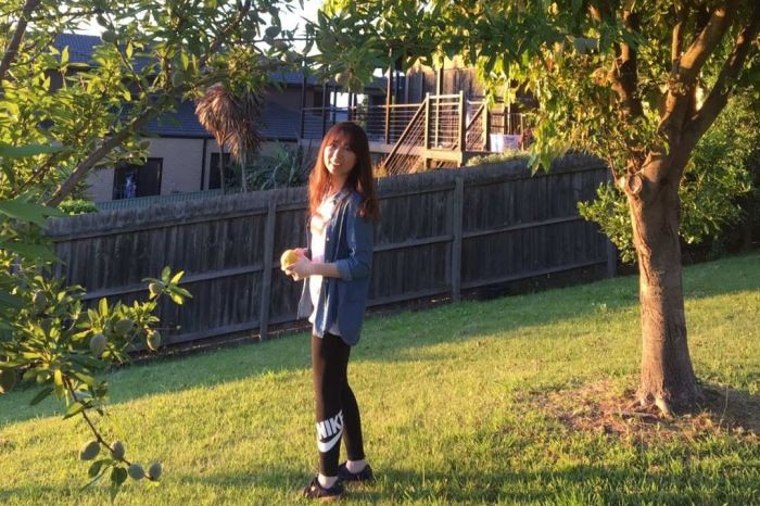 Linda Yang stands in a backyard holding a mango.