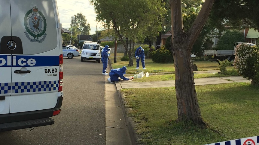 Three forensic officers examining the front lawn on a house.