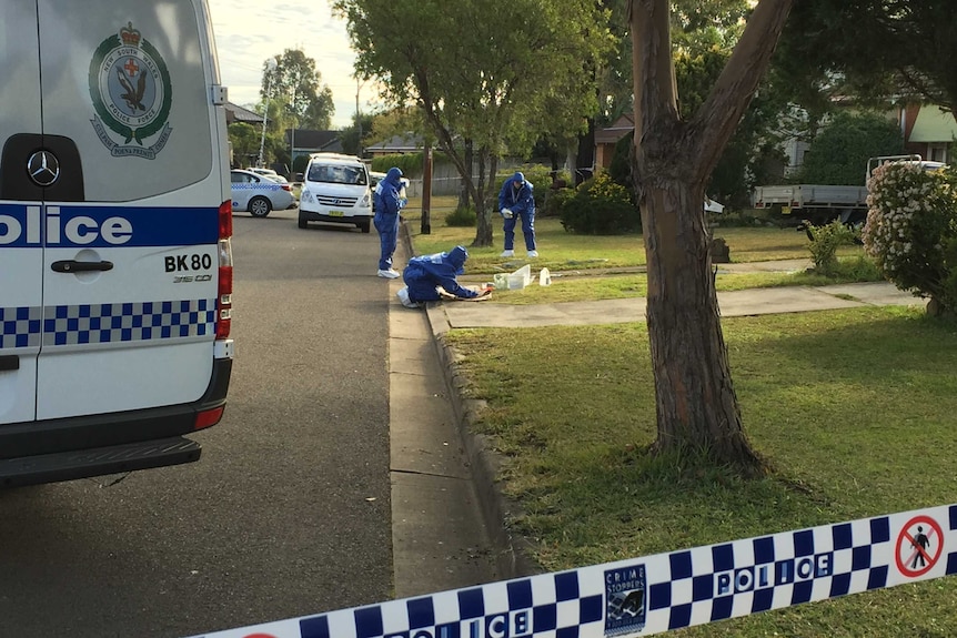 Three forensic officers examining the front lawn on a house.