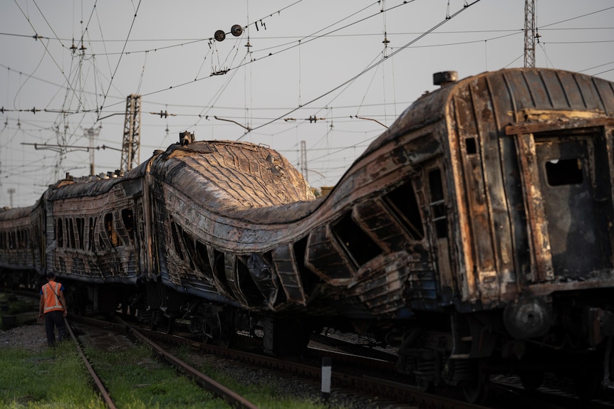 Un feroviar stă lângă un tren care a fost grav avariat după un atac rusesc.