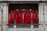 Naked people stand on balconies draped in red veils.