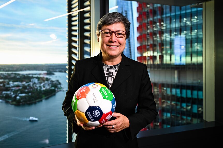 A woman holds a soccer ball and smiles.