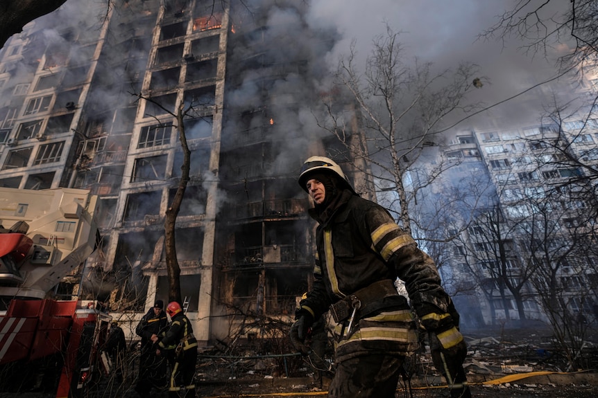 A firefighter walks outside a destroyed apartment building, with smoke billowing from many charred flats.