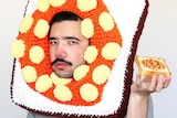 A man with a moustache holds up beans on toast, while wearing a crocheted headpiece in the shape of beans on toast