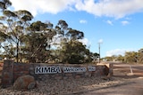 A sign on a short stone wall reading "Kimba welcomes you".