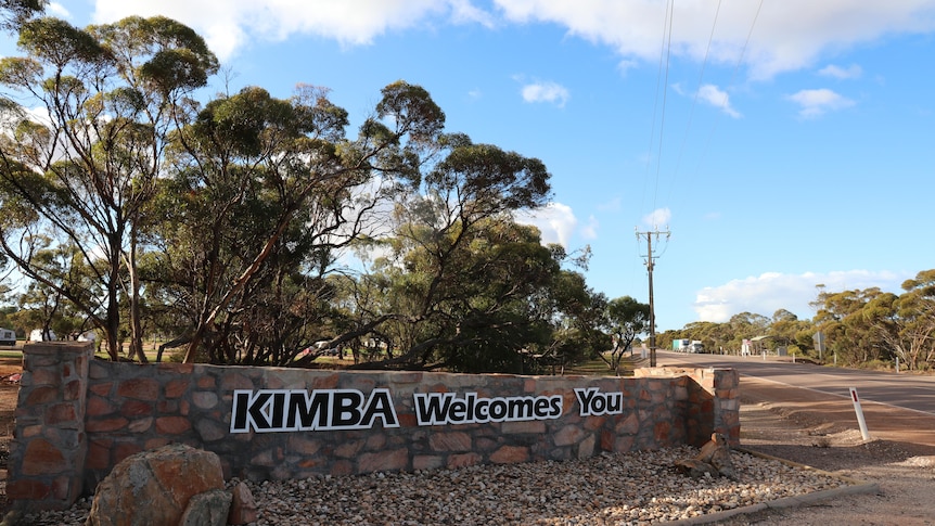 A sign on a short stone wall reading "Kimba welcomes you".