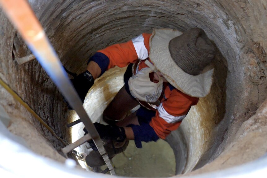 Une femme descendant une échelle dans un puits de mine étroit.