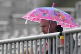 A man hold a pink umbrella behind a railing.