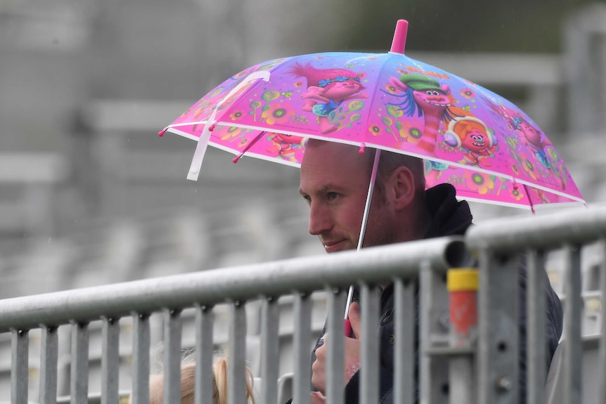 A man hold a pink umbrella behind a railing.
