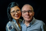 Caucasian man and Asian woman in an embrace looking at the camera.