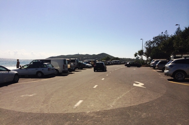 Cars parked on the Byron Bay beachfront with the lighthouse in the background.