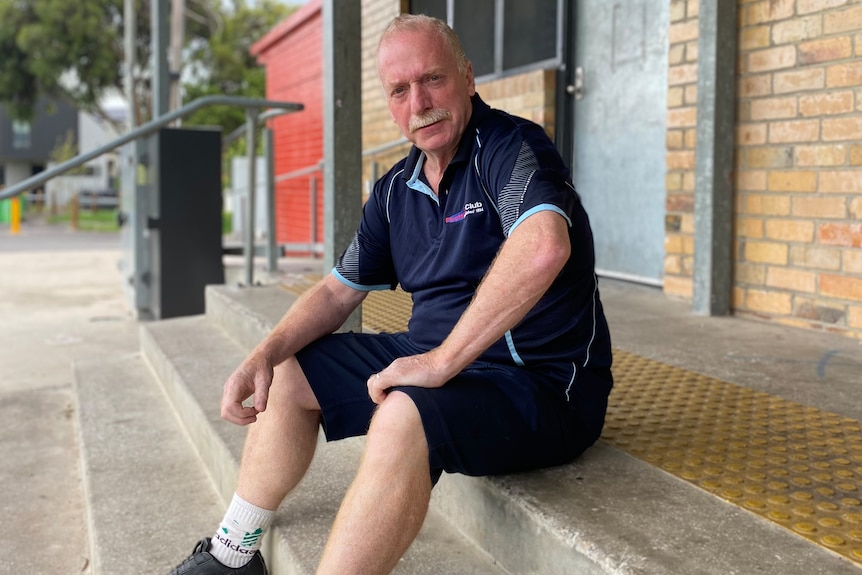 Older man wearing shorts sits on steps to entrance of a building.