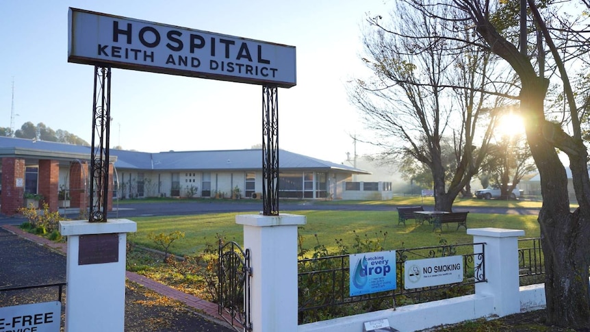 A sign reading 'Keith and District Hospital' stands in front of a grassy lawn and long brick building.