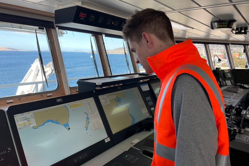 A man in hi vis looks at screens on a ship