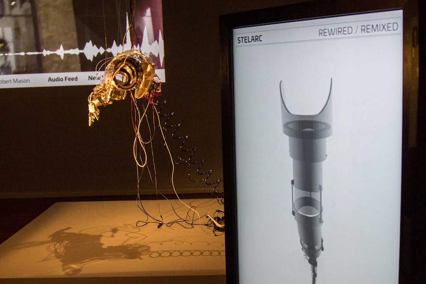 Stelarc's robotic arm hangs in the gallery beside a touch screen that visitors can use to manipulate it.