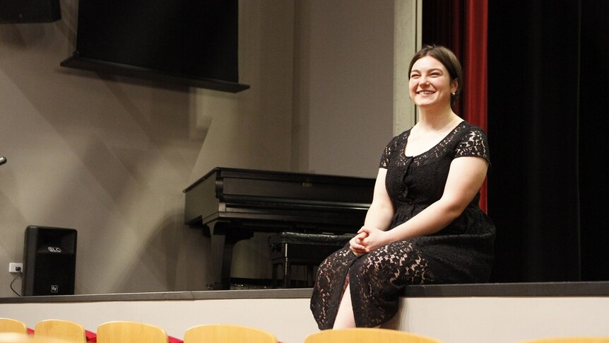 Young woman sits on a stage in a black dress