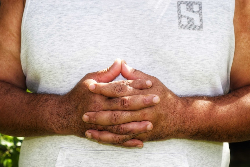 A man wearing a singlet interlaces his fingers as he holds his hands in front of his waist.