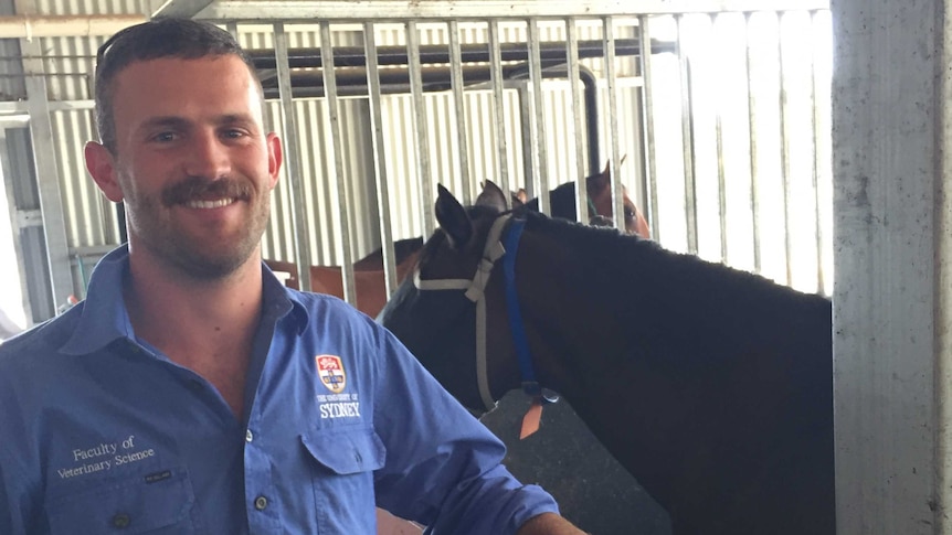 University vet student Tim Barton stand smiling beside a horse stable