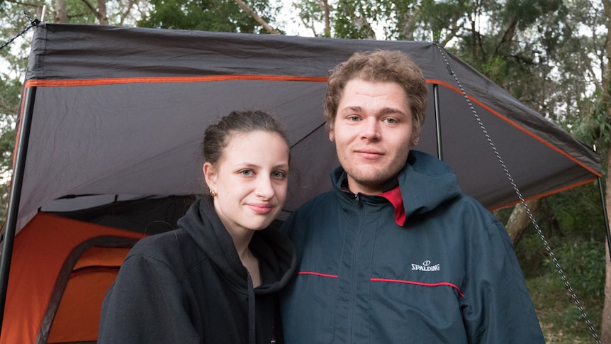 A young couple stand outside a tent