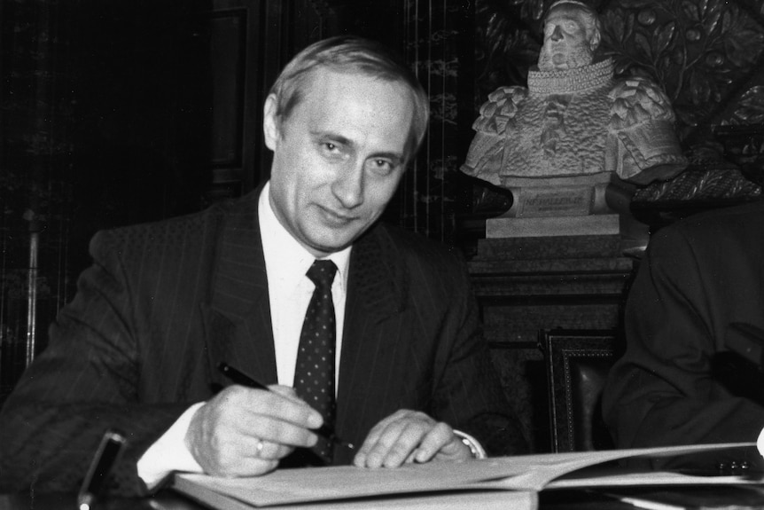 Two men sit at a table, signing documents.