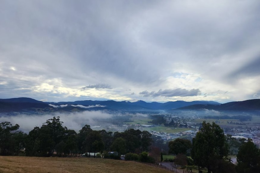 mist clings to rolling green hills and a small town 