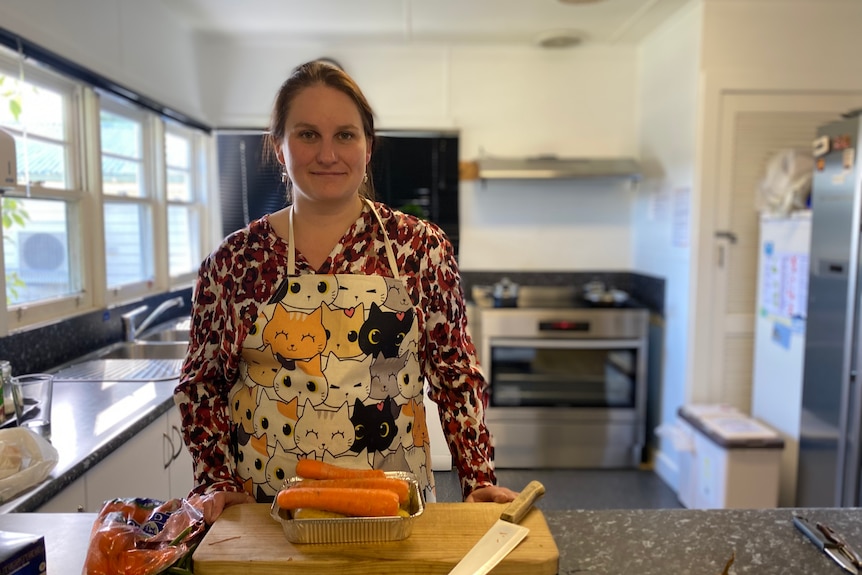 Casey smiles at the camera as she stands in a kitchen, preparing a meal.