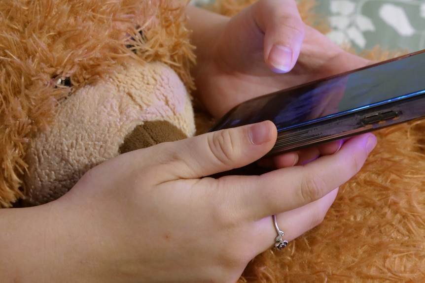 Hands hold a phone while cuddling a teddy bear