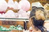 A woman stands in front of a shelf of rose quartz, inspecting one crystal in her hand.