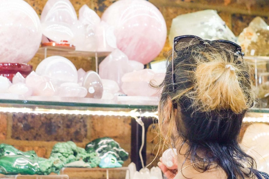 A woman stands in front of a shelf of rose quartz, inspecting one crystal in her hand.