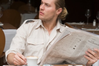 A man reads the paper at an outdoor coffee shop.