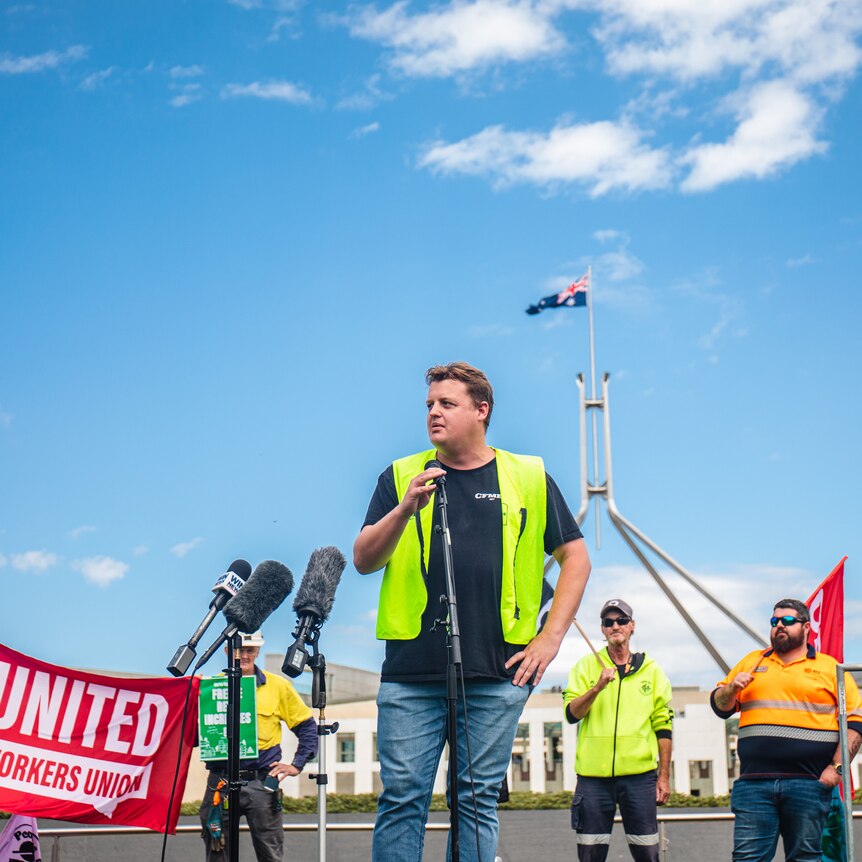 A man in front of union banners standing with a microphone