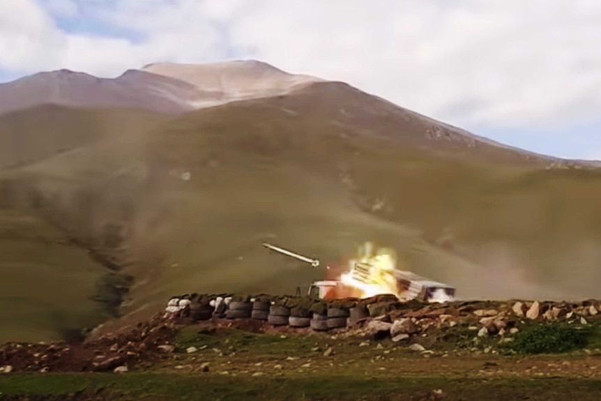 A still image of a missile being shot from a tank with mountains in the background.