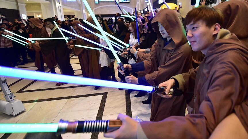 South Korean Star Wars fans hold their lightsabers in a cinema foyer.