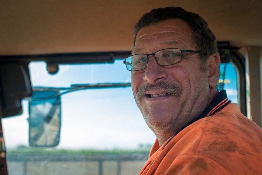 Cane harvester driver Alf Delorenzi smiles from inside the cabin of his harvester.