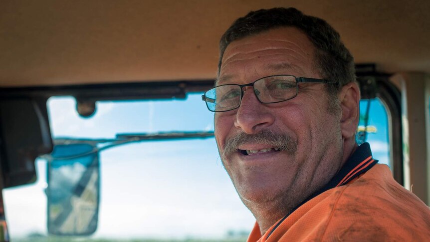 Cane harvester driver Alf Delorenzi smiles from inside the cabin of his harvester.