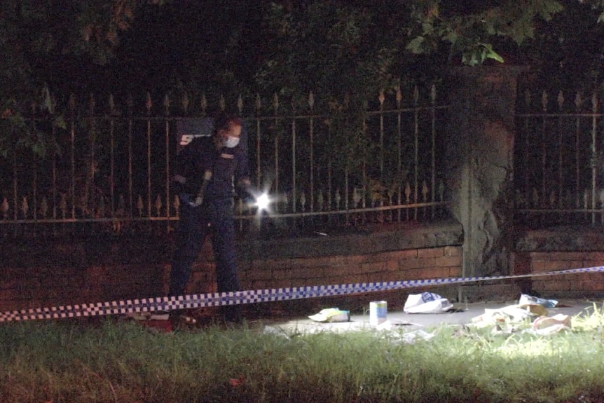 Police shine torches behind police tape at a crime scene.